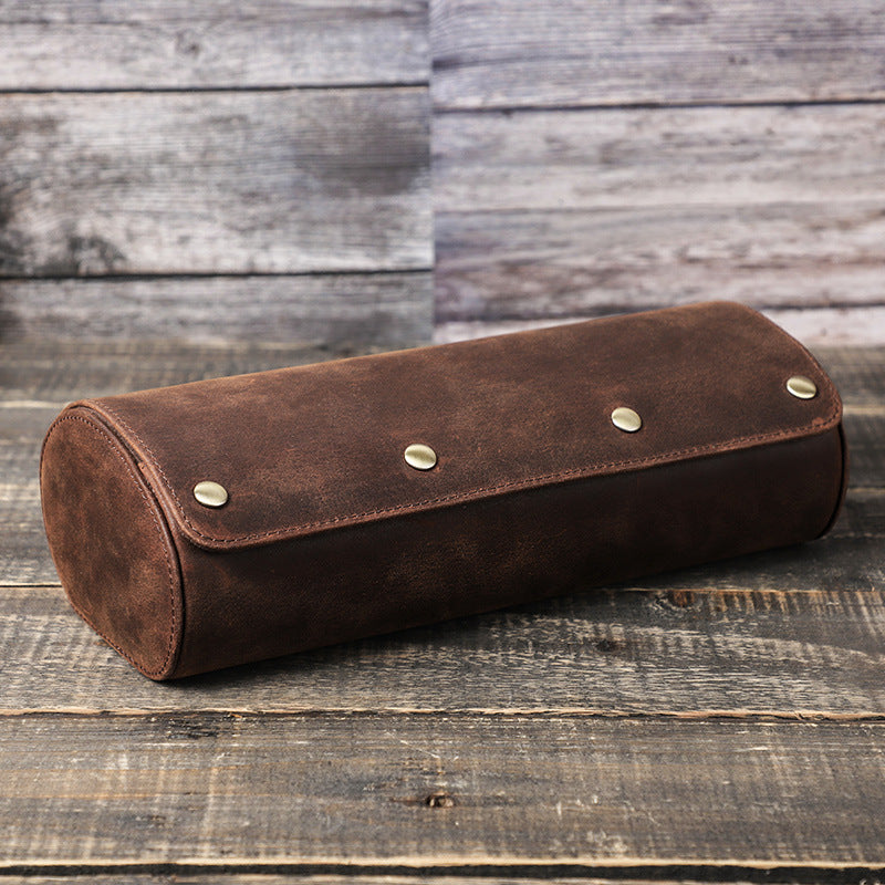 Brown leather watch case cylindrical pouch with metal studs on a wooden surface