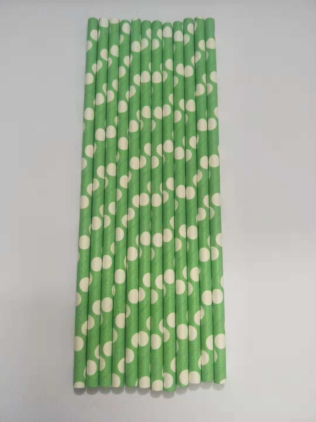 A set of paper straws with a green and white polka dot pattern, arranged vertically on a plain light gray background.