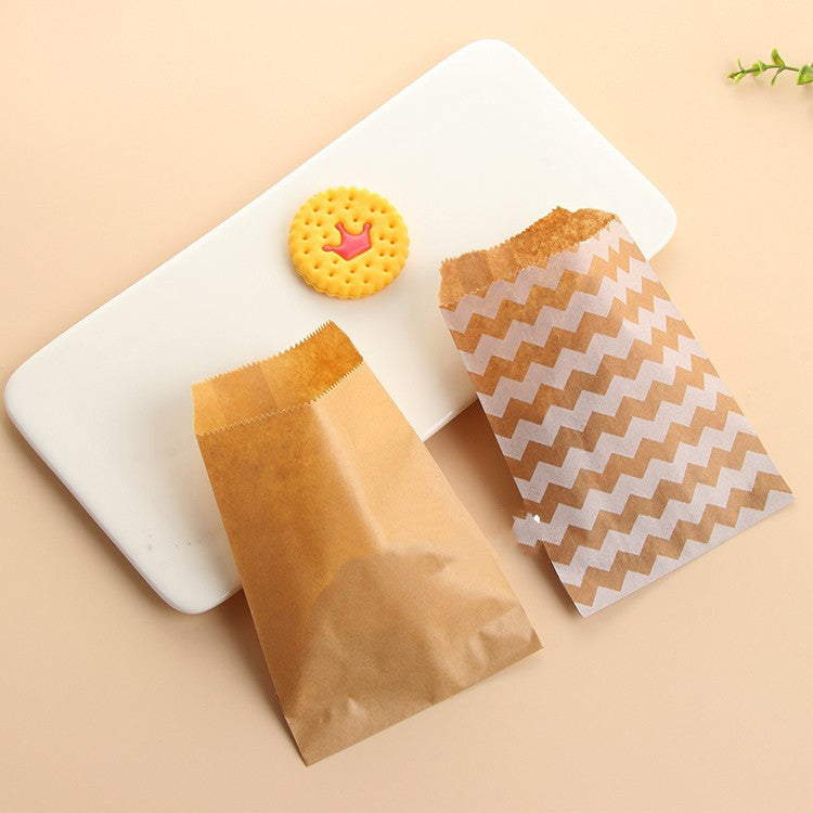 Two paper bags, one brown and one with a zigzag pattern, on a beige surface with a white cutting board and a cookie.