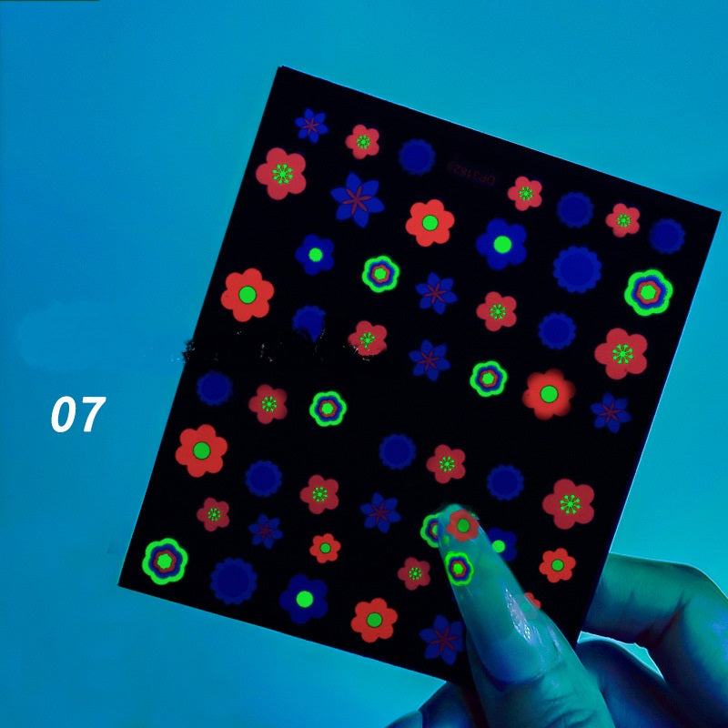 Fluorescent stickers on a black sheet held by a hand with blue nail polish against a blue background.