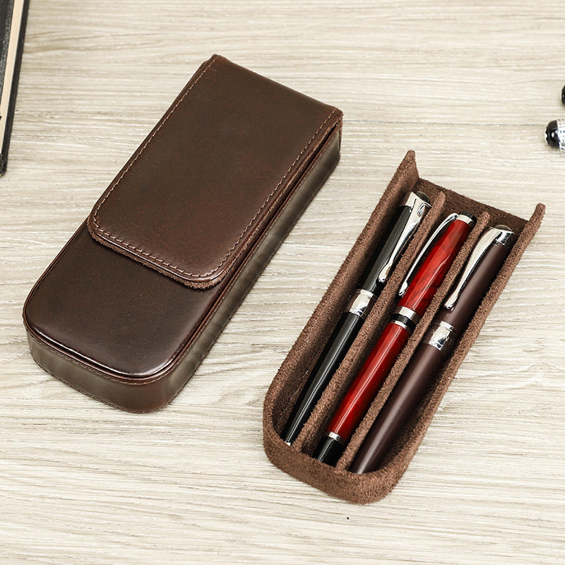 Brown leather pen case with three pens on a light wooden surface