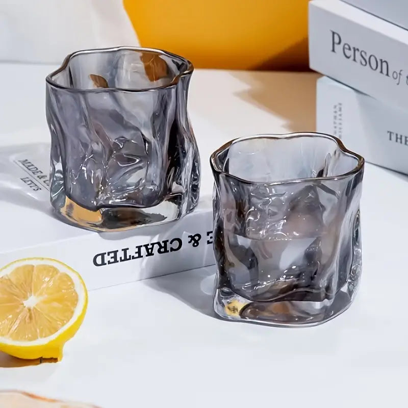 Two black glass shot glasses on a white surface with a lemon and books in the background.