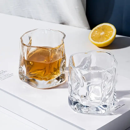 Two clear glasses with one containing a yellow liquid and the other empty, on a white surface with a lemon half.
