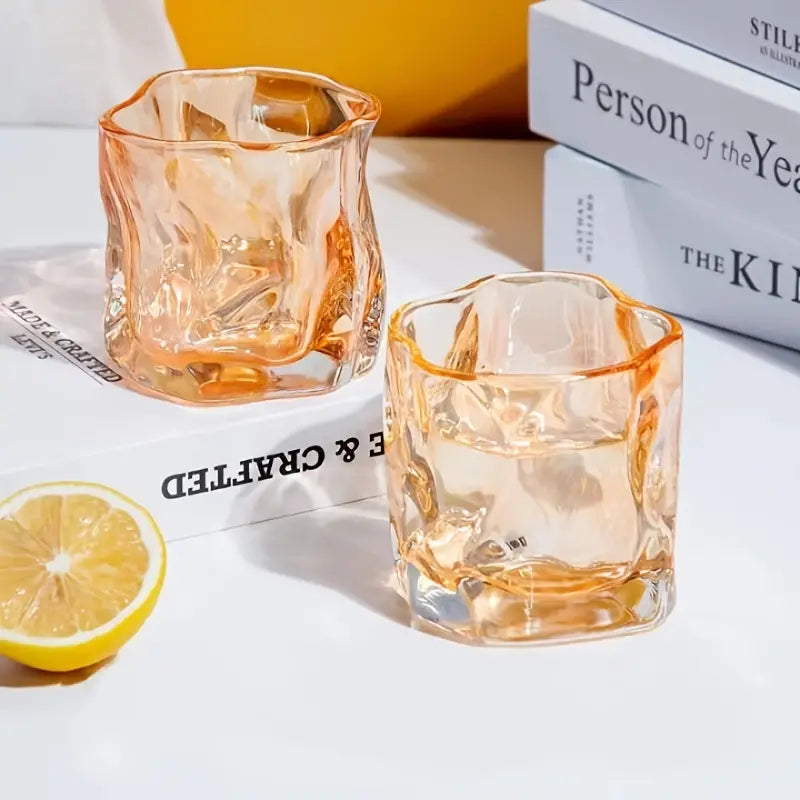 Two orange-tinted glass tumblers with a lemon on a white surface.