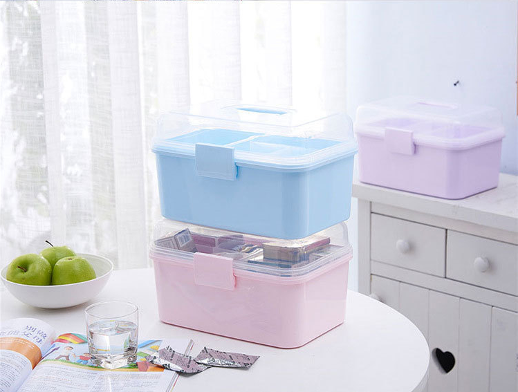 Three plastic storage containers stacked on a white table in a bright room. The stack includes a lavender container on top, a light blue one in the middle, and a pink one at the bottom, all with clear lids.