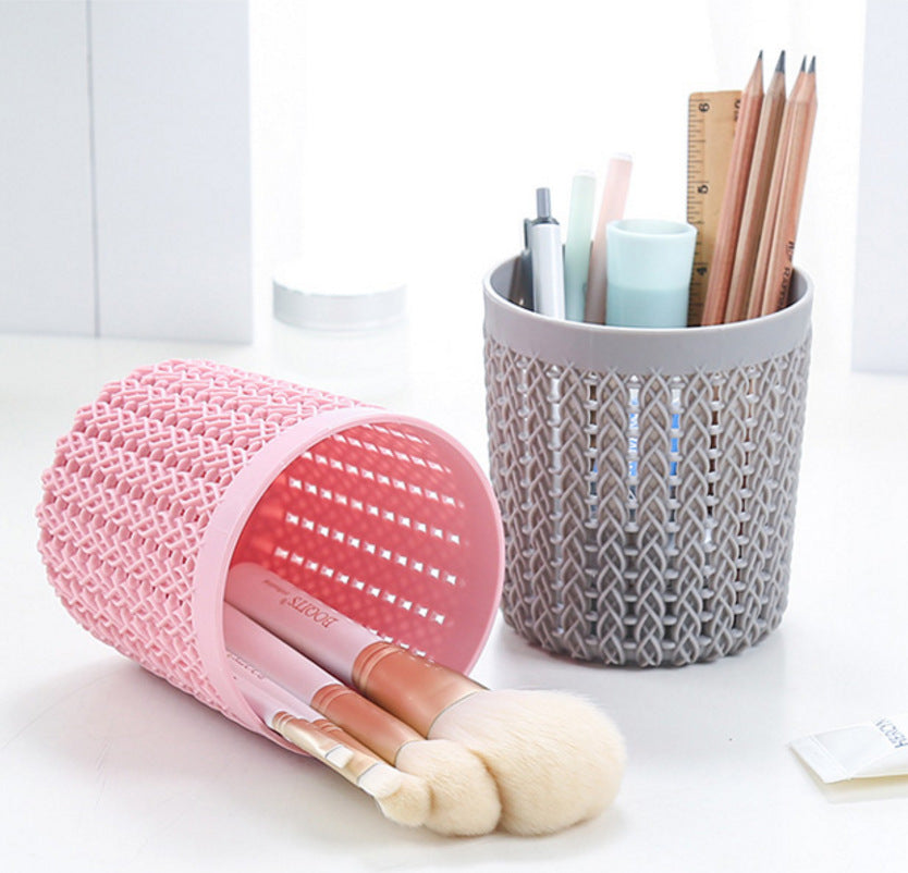 Pink mesh container with makeup brushes and gray woven container with stationery items on a white surface.