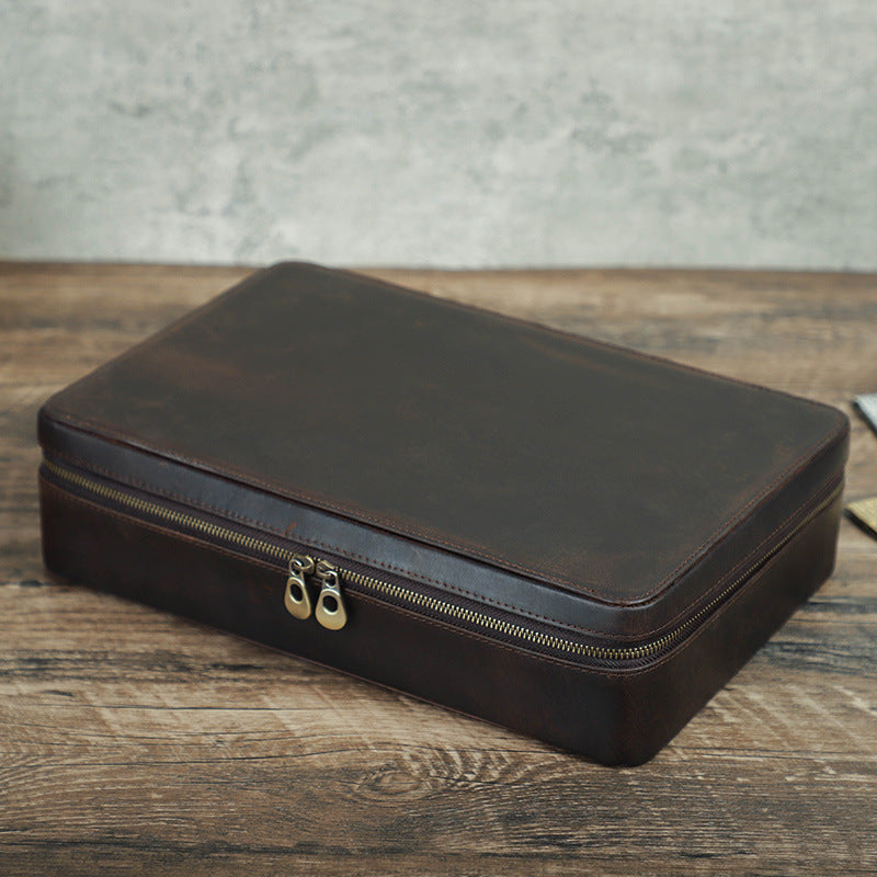 Brown leather watch travel case with gold zipper on a wooden surface