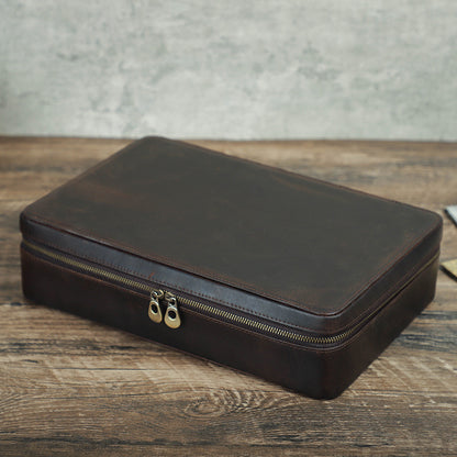 Brown leather watch travel case with gold zipper on a wooden surface